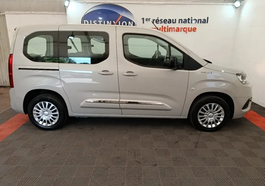 Vue de profil côté droit d'un Toyota Proace City Verso électrique gris clair avec jantes argentées en intérieur showroom.