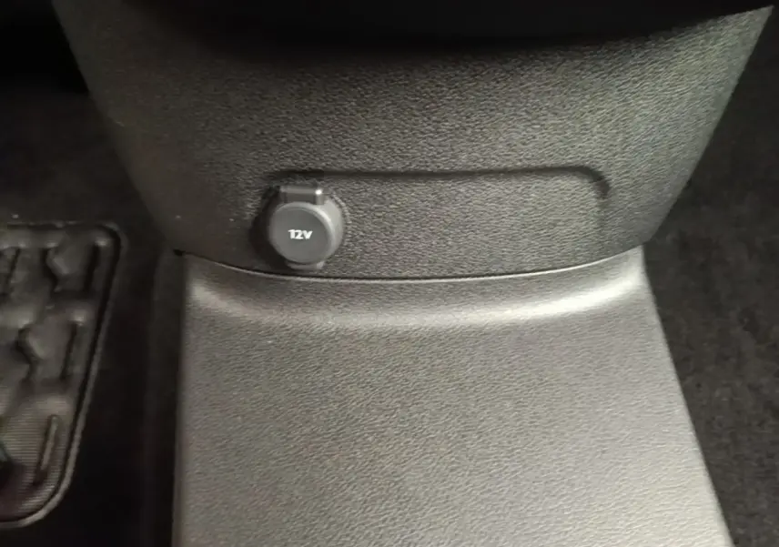 Prise 12V noire en gros plan sur la console centrale d’un Toyota Proace City Verso gris clair, vue intérieure basse.