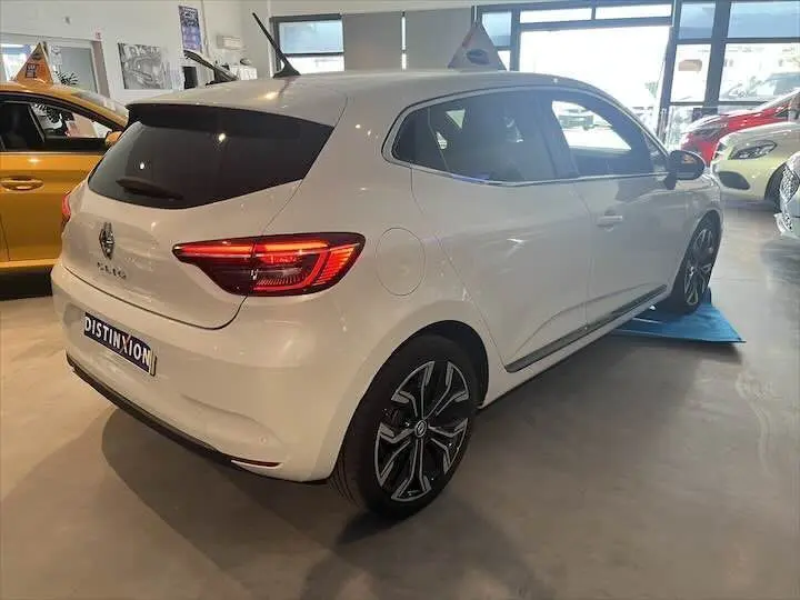 Vue 3/4 arrière droite d'une Renault Clio V blanche nacrée avec jantes alliage et vitres teintées en showroom.
