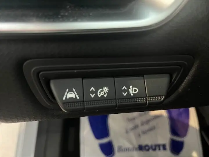 Gros plan sur les commandes d'assistance et éclairage de la Renault Clio V blanche nacrée, côté conducteur.