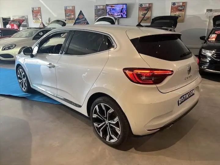 Renault Clio V blanc nacré métal vue 3/4 arrière droit en intérieur avec jantes alliage et vitres teintées.