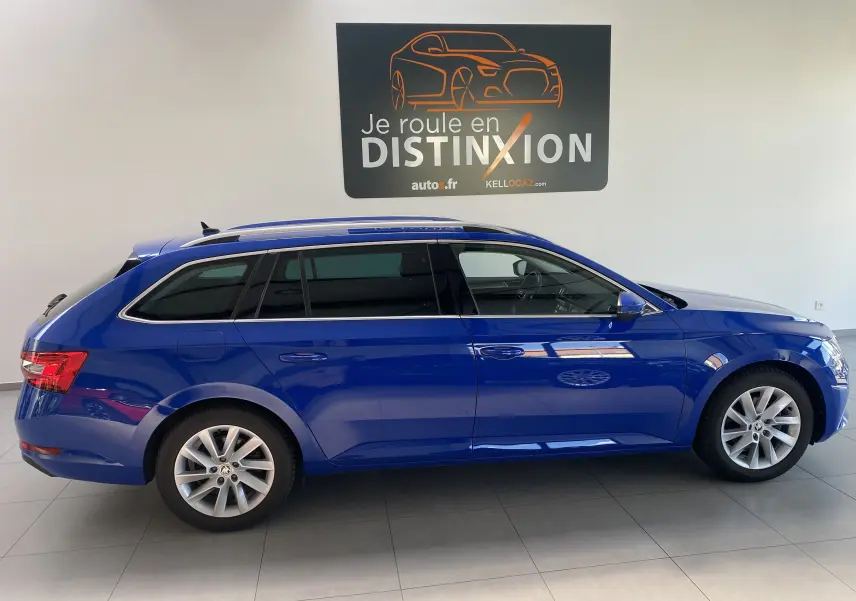 Vue de profil côté gauche d'une Skoda Superb Combi bleu énergie en hybride rechargeable, stationnée en intérieur.