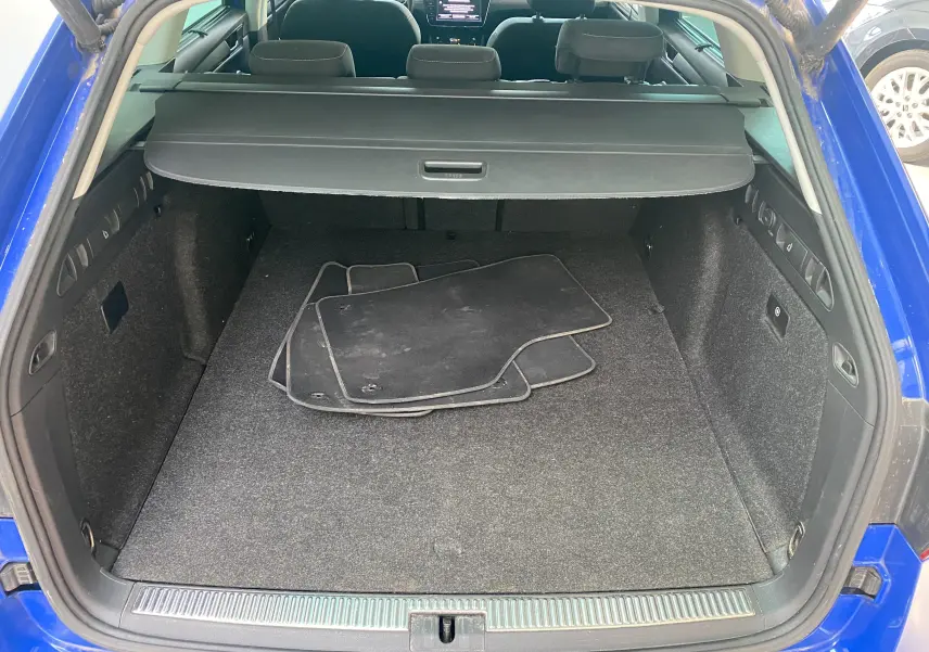 Coffre ouvert d'une Skoda Superb Combi bleu énergie, montrant un espace de chargement avec tapis de sol noirs et cache-bagages.