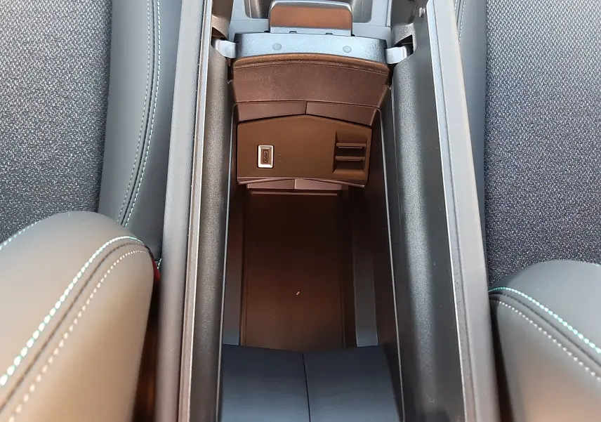 Vue plongeante sur le rangement central ouvert entre les sièges noirs avec surpiqûres bleues d'une Peugeot 308 2025.