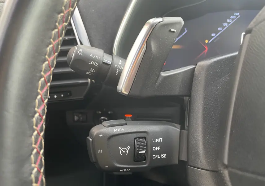 Gros plan sur les commandes au volant du DS7 gris, mettant en valeur le régulateur de vitesse et la manette des phares.