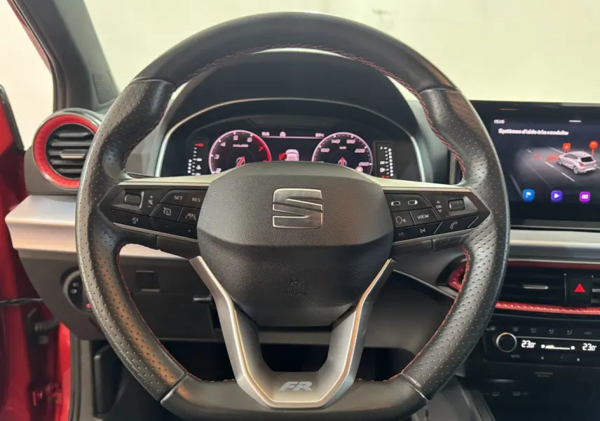 Vue rapprochée du volant cuir perforé avec logo SEAT et badge FR, tableau de bord et écran tactile visibles en arrière-plan.