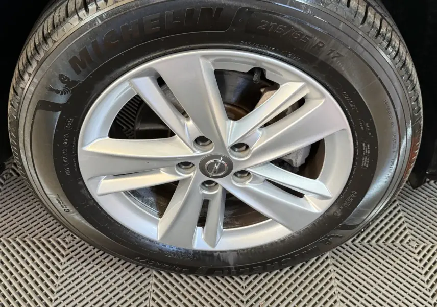 Gros plan sur la roue avant droite d’un Opel Grandland X noir, jante alliage argentée avec logo Opel central.