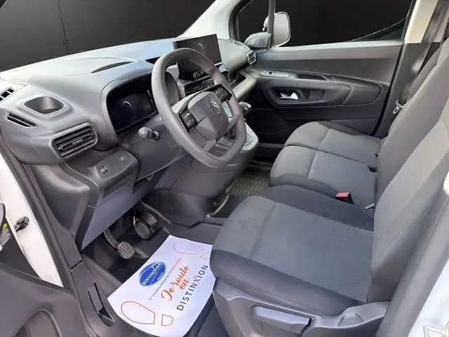 Vue intérieure côté conducteur du Citroën Berlingo blanc 2025, montrant le tableau de bord et les sièges avant en tissu gris.