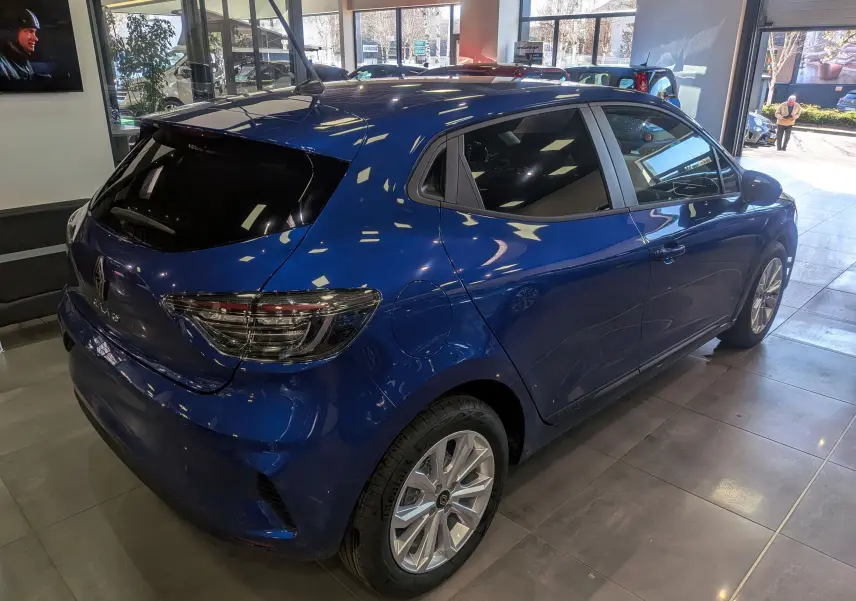 Vue 3/4 arrière droite d'une Renault Clio V Bleu Iron en intérieur, avec vitres teintées et jantes alliage 16 pouces.