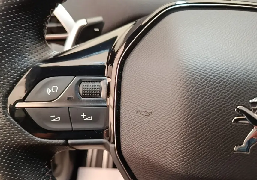 Gros plan sur les commandes gauche du volant cuir du Peugeot 3008 hybride bleu, avec logo lion visible.