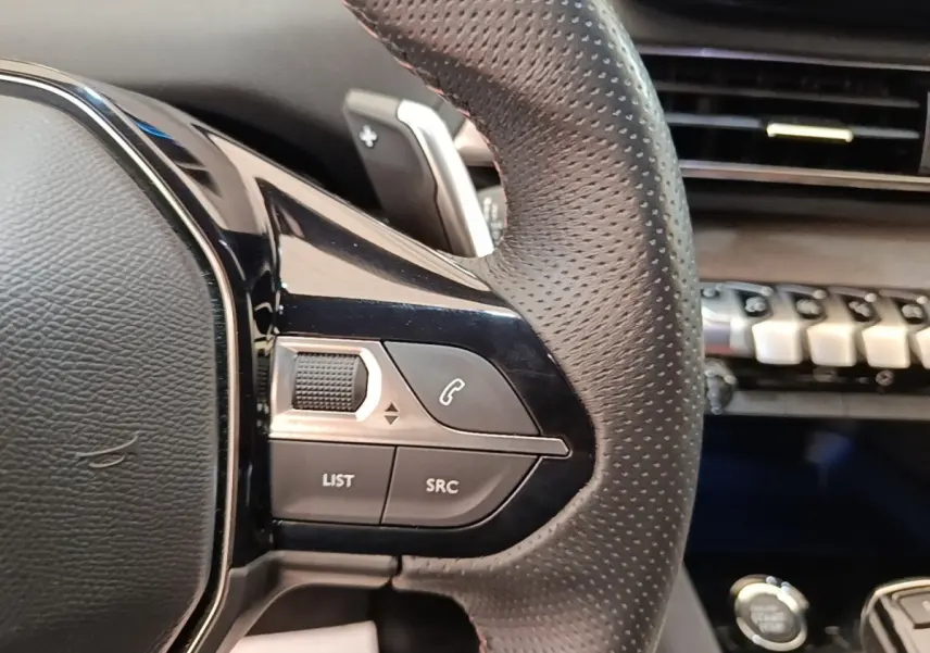 Gros plan sur le volant cuir perforé côté gauche du Peugeot 3008 bleu avec commandes audio et téléphone intégrées.