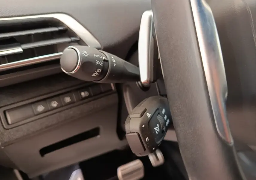 Gros plan sur la commande des phares et volant en cuir noir du Peugeot 3008 hybride bleu, intérieur côté gauche.