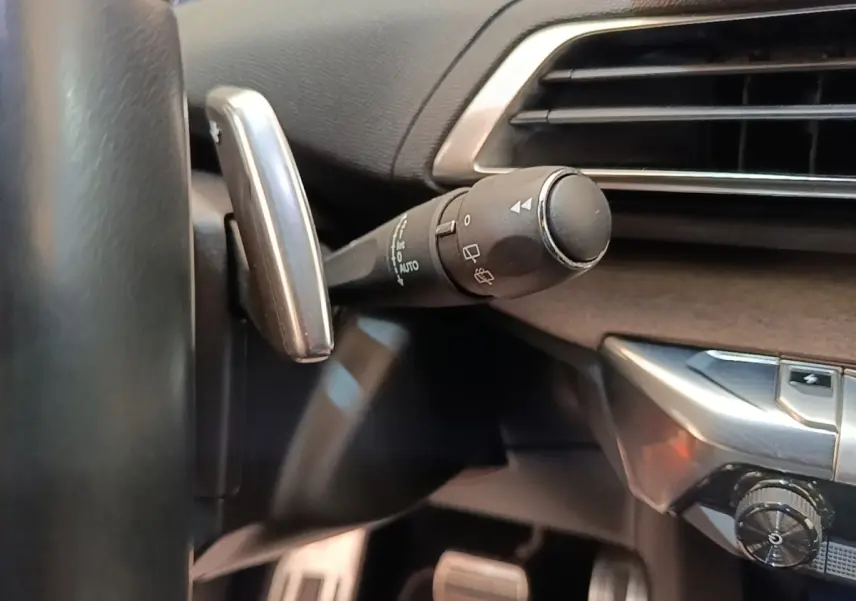 Gros plan sur la manette de commande des essuie-glaces côté gauche du tableau de bord noir du Peugeot 3008 bleu hybride.