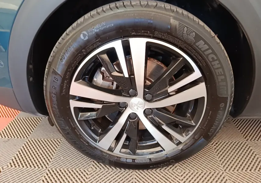 Gros plan sur la roue avant droite d’un Peugeot 3008 bleu 1.6 Hybrid 225 GT avec jante alliage bicolore.