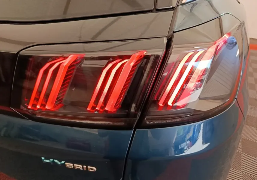 Gros plan sur le feu arrière droit rouge du Peugeot 3008 hybride bleu, avec logo HYBRID visible sur la carrosserie.