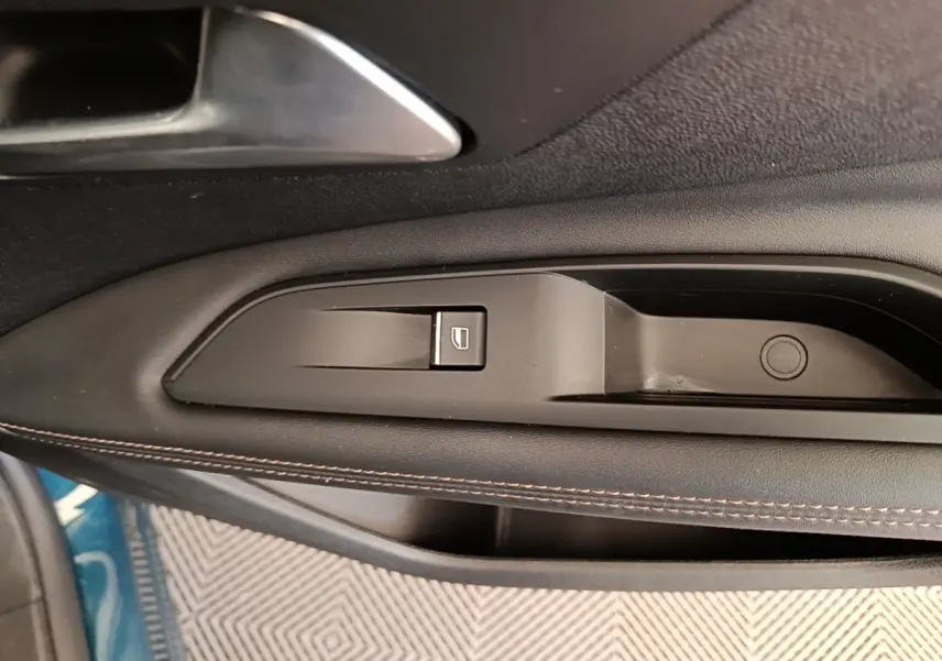 Gros plan sur la commande de lève-vitre côté gauche en plastique noir avec surpiqûres marron, intérieur Peugeot 3008 bleu visible.