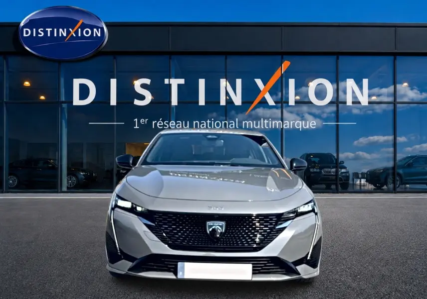 Vue avant d'une Peugeot 308 gris métallisé 2025 avec calandre noire et phares LED fins, devant une vitrine Distinxion.