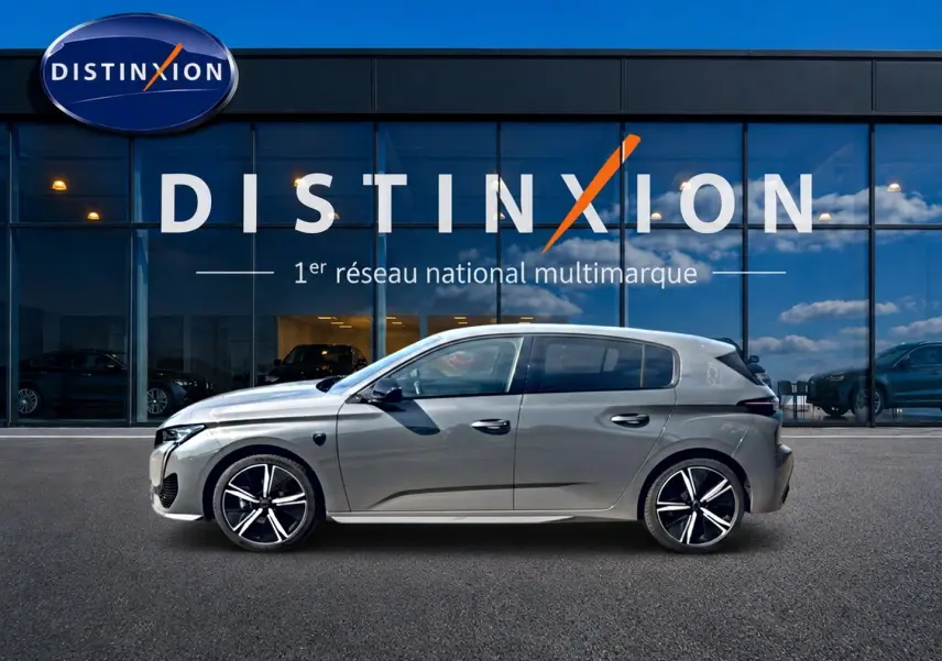Profil droit d’une Peugeot 308 gris métallisé 2025 avec jantes alliage noires devant un showroom Distinxion.