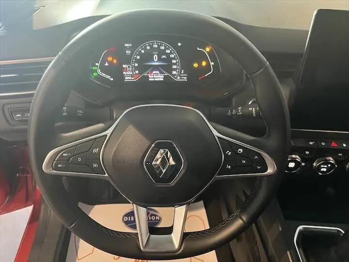 Vue rapprochée du volant noir de la Renault Clio V 1.0 TCE 90 CH Intens rouge flamme, avec tableau de bord digital allumé.