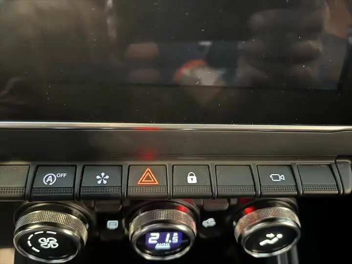 Gros plan sur la console centrale de la Renault Clio V rouge flamme, montrant les commandes de climatisation et boutons fonctionnels.