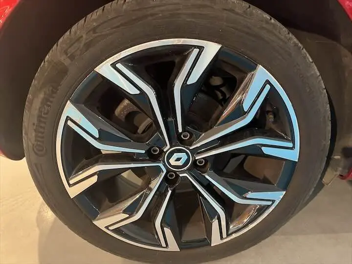 Gros plan sur la jante alliage noire et argentée avec logo Renault au centre d'une Renault Clio V rouge flamme.