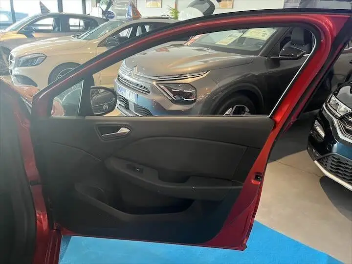 Porte avant gauche ouverte d'une Renault Clio V rouge flamme métal, intérieur noir visible en concession.