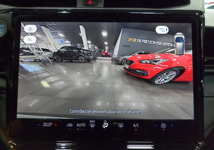 Écran de caméra de recul affichant un parking intérieur avec plusieurs voitures, vue depuis un Ford Puma gris.