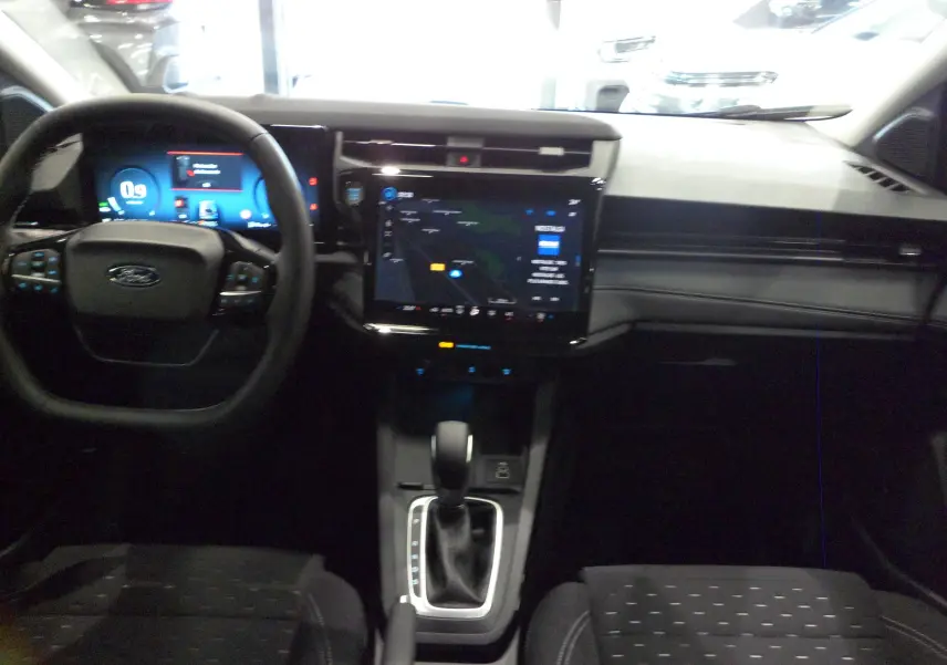 Vue intérieure avant du Ford Puma 2025 avec tableau de bord numérique, écran tactile central et sellerie tissu noire.