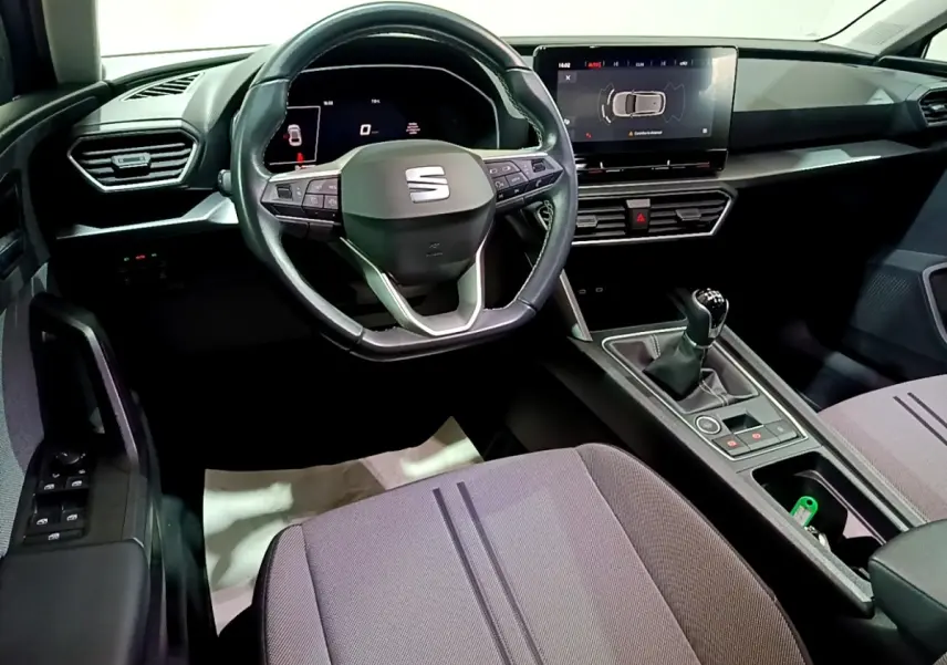 Vue intérieure du poste de conduite du SEAT Leon 2023, volant cuir multifonctions et écran tactile central visible.