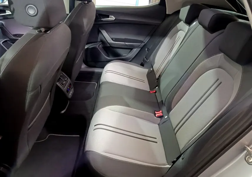 Vue intérieure arrière de la SEAT LEON 2023 montrant la banquette bicolore gris clair et foncé avec ceintures rouges.
