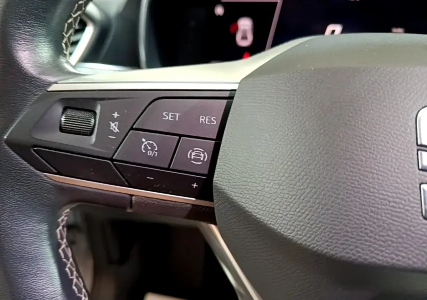 Gros plan sur les commandes à gauche du volant cuir noir du SEAT LEON gris clair 2023, boutons de régulateur de vitesse et assistance conduite.