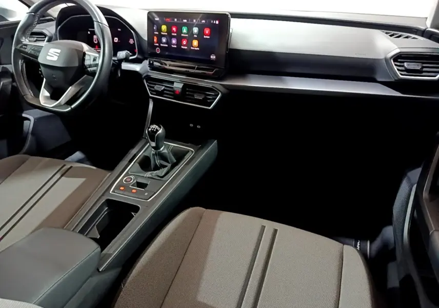 Intérieur avant de la SEAT LEON 2023, vue côté passager, tableau de bord noir avec écran tactile et levier de vitesses manuel.