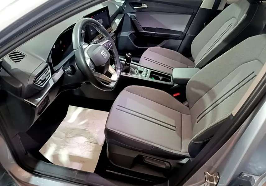Vue intérieure côté conducteur de la SEAT LEON gris clair 2023, montrant sièges tissu et tableau de bord digital.