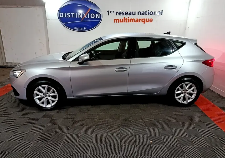 Profil côté gauche d'une SEAT LEON gris clair 2023 garée en intérieur avec jantes alliage et feux arrière allumés.