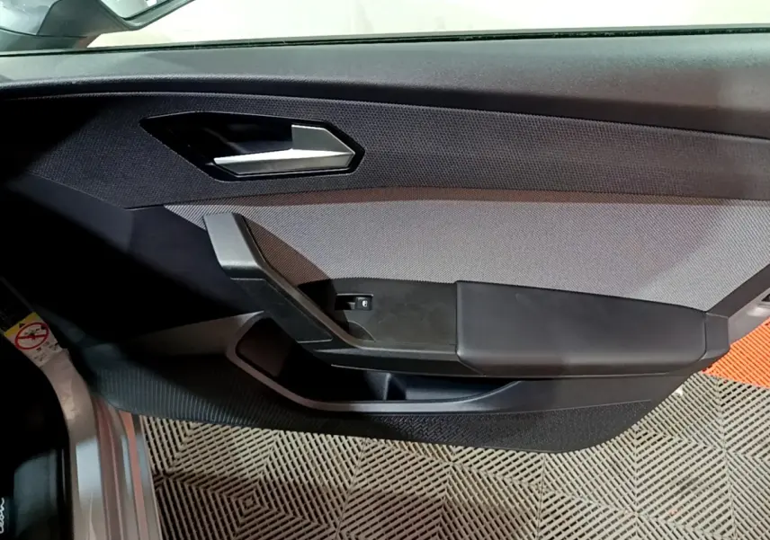 Panneau de porte côté gauche gris et noir de la SEAT LEON 2023 avec poignée argentée et bouton de vitre électrique.