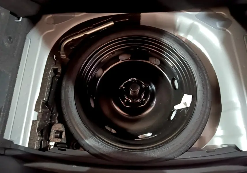 Roue de secours galette noire dans le coffre d'une SEAT Leon 2023, vue plongeante sur le pneu et son emplacement.