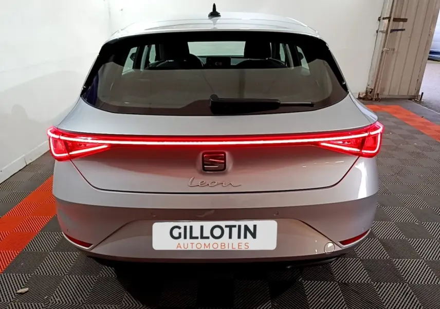 Vue arrière d'une SEAT Leon gris clair 2023 avec feux arrière LED allumés et plaque GILLOTIN Automobiles.