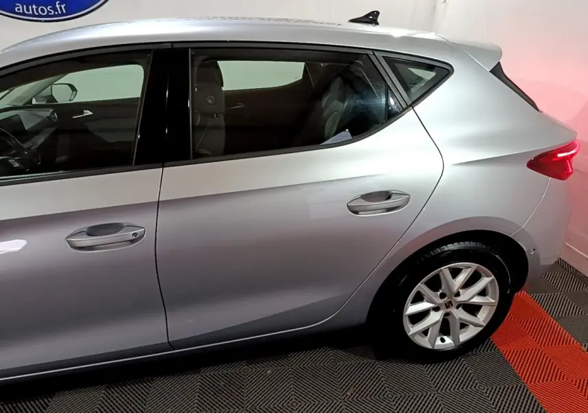 Vue latérale côté gauche d'une SEAT Leon gris clair 2023 avec jantes alliage et vitres teintées.