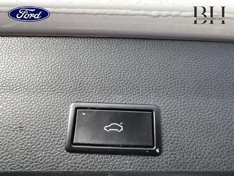 Bouton noir d'ouverture du hayon sur tableau de bord en cuir noir, intérieur d'une SEAT Ateca blanc Nevada.