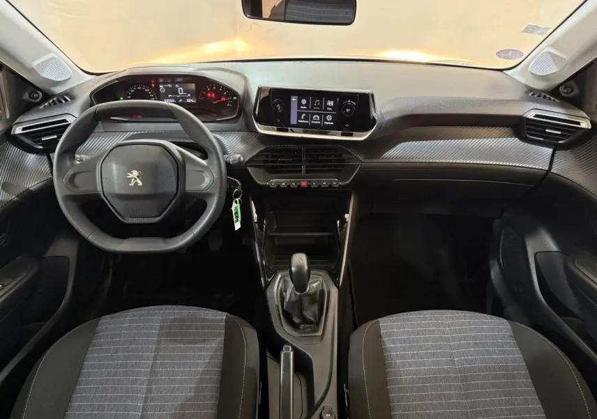 Vue intérieure avant de la Peugeot 208 PureTech 75 S&S Like 2020, tableau de bord noir avec écran tactile central et volant compact.
