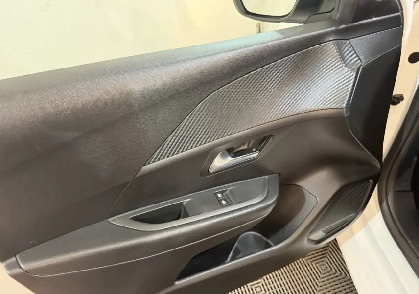 Vue rapprochée de la porte avant gauche noire avec insert effet carbone et commandes de lève-vitres d'une Peugeot 208 2020.