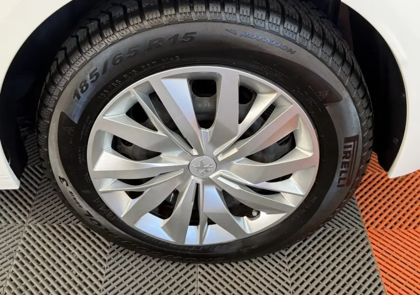 Gros plan sur la roue avant droite d'une Peugeot 208 blanche, mettant en valeur la jante argentée et le pneu Pirelli.