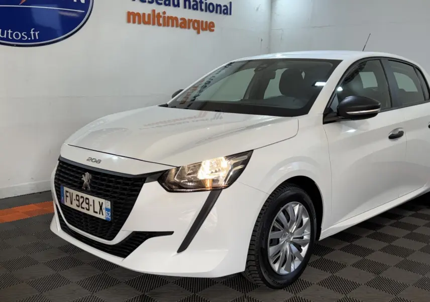 Peugeot 208 blanche vue 3/4 avant droit, phare allumé et calandre noire distinctive sur fond intérieur showroom.