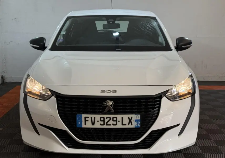 Vue frontale d'une Peugeot 208 blanche avec phares allumés et calandre noire distinctive.