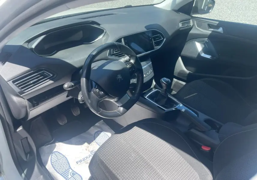Vue intérieure côté conducteur du Peugeot 308 blanc, montrant le volant compact, la boîte manuelle et la console centrale moderne.