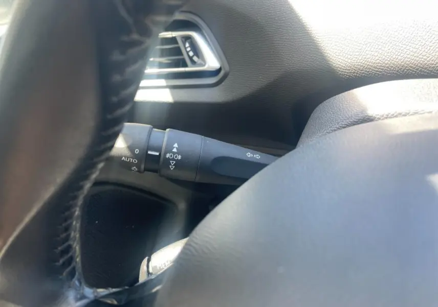 Détail du commodo d’éclairage côté gauche du volant dans l’habitacle d’une Peugeot 308 blanche de 2020.