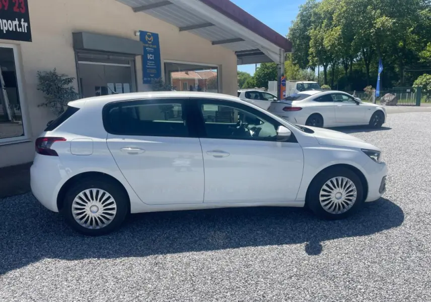Peugeot 308 blanc vue de profil côté gauche, avec jantes à enjoliveurs et carrosserie 5 portes sous un ciel dégagé.