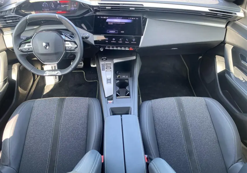 Vue intérieure avant de la Peugeot 308 1.2 hybrid 145 GT e-dcs6 2025, montrant sièges noirs, volant multifonction et écran tactile central.