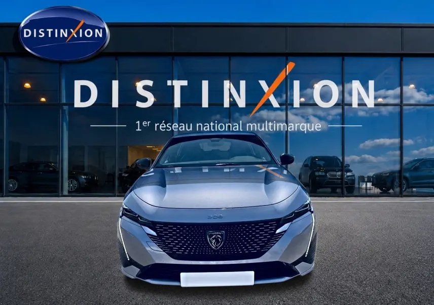Vue frontale d'une Peugeot 308 gris métallisé 2025 avec calandre noire et logo lion distinctif, devant un showroom Distinxion.