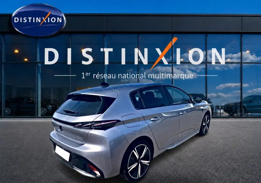 Peugeot 308 gris vue 3/4 arrière droit, avec jantes alu et feux arrière à LED, devant un showroom Distinxion.